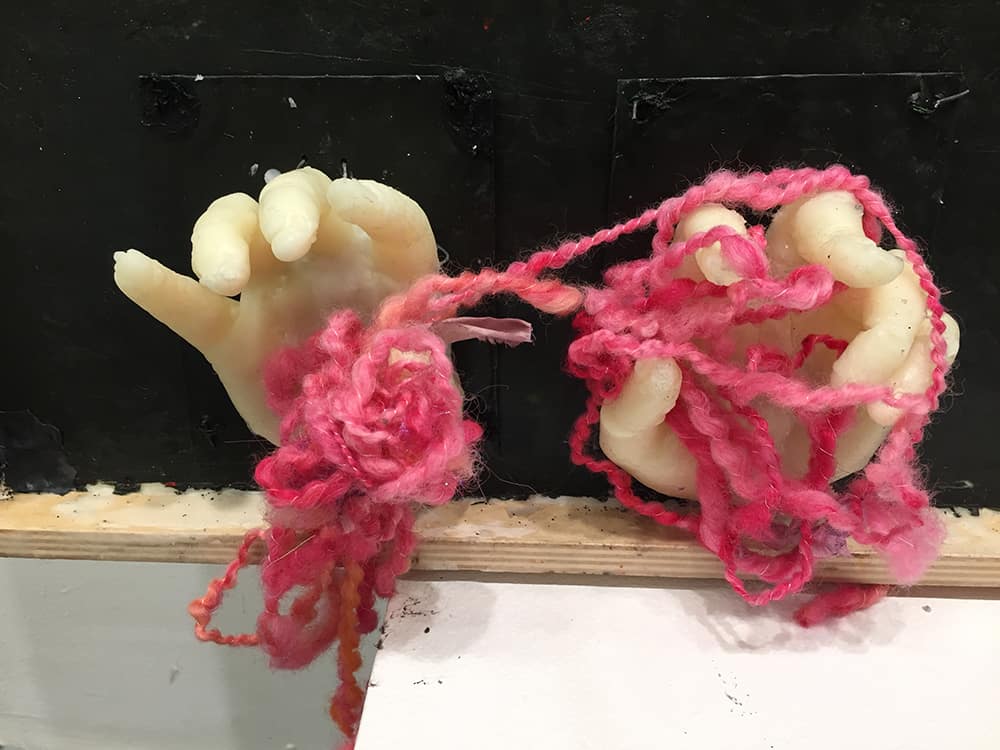 wax encaustic detail of hands knitting one of the eponymous pink hats from the Women's March 2017